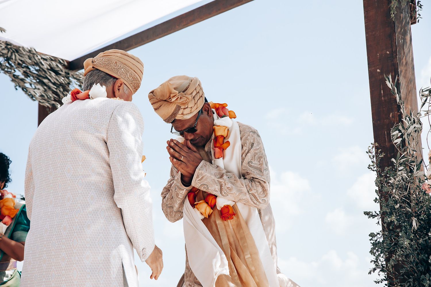 Traditional Indian wedding ceremony with participants in white and red attire under a bright sky.