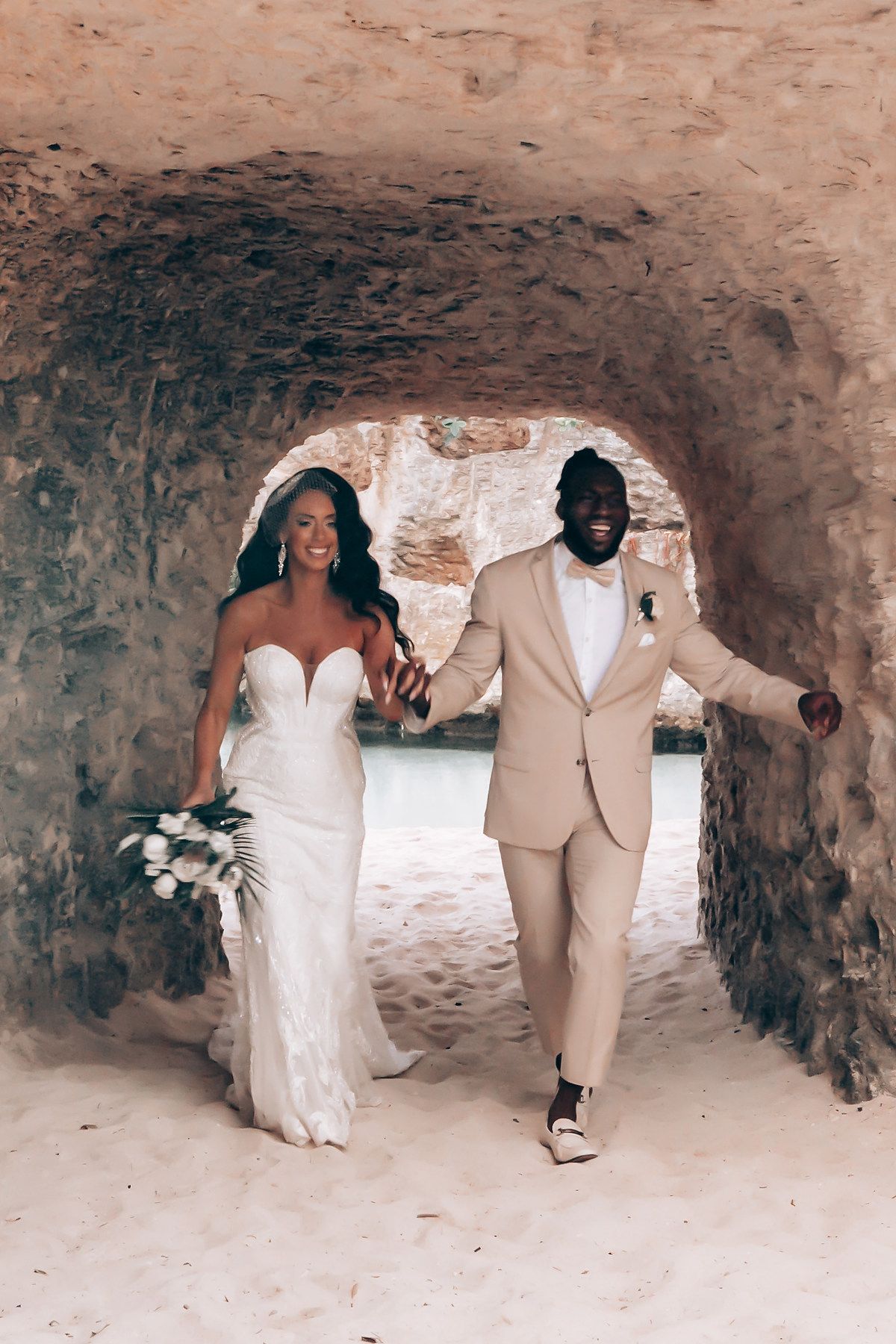 Wedding couple celebrates in stone cave tunnel wearing white dress and tan suit.