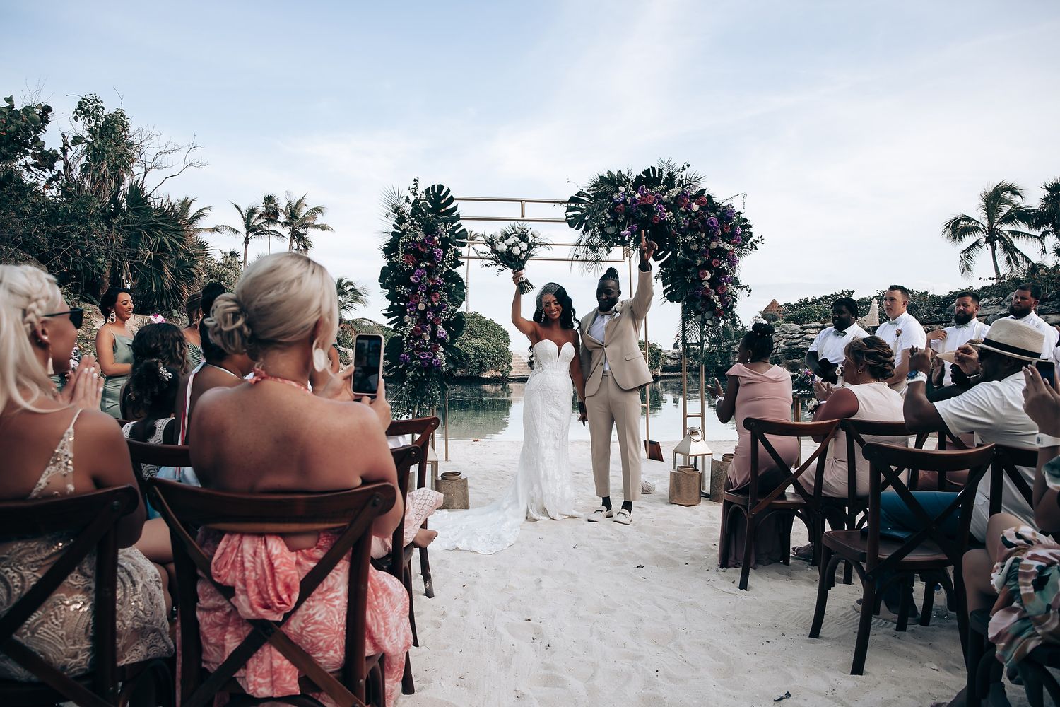 Outdoor beach wedding ceremony with floral arch and seated guests.