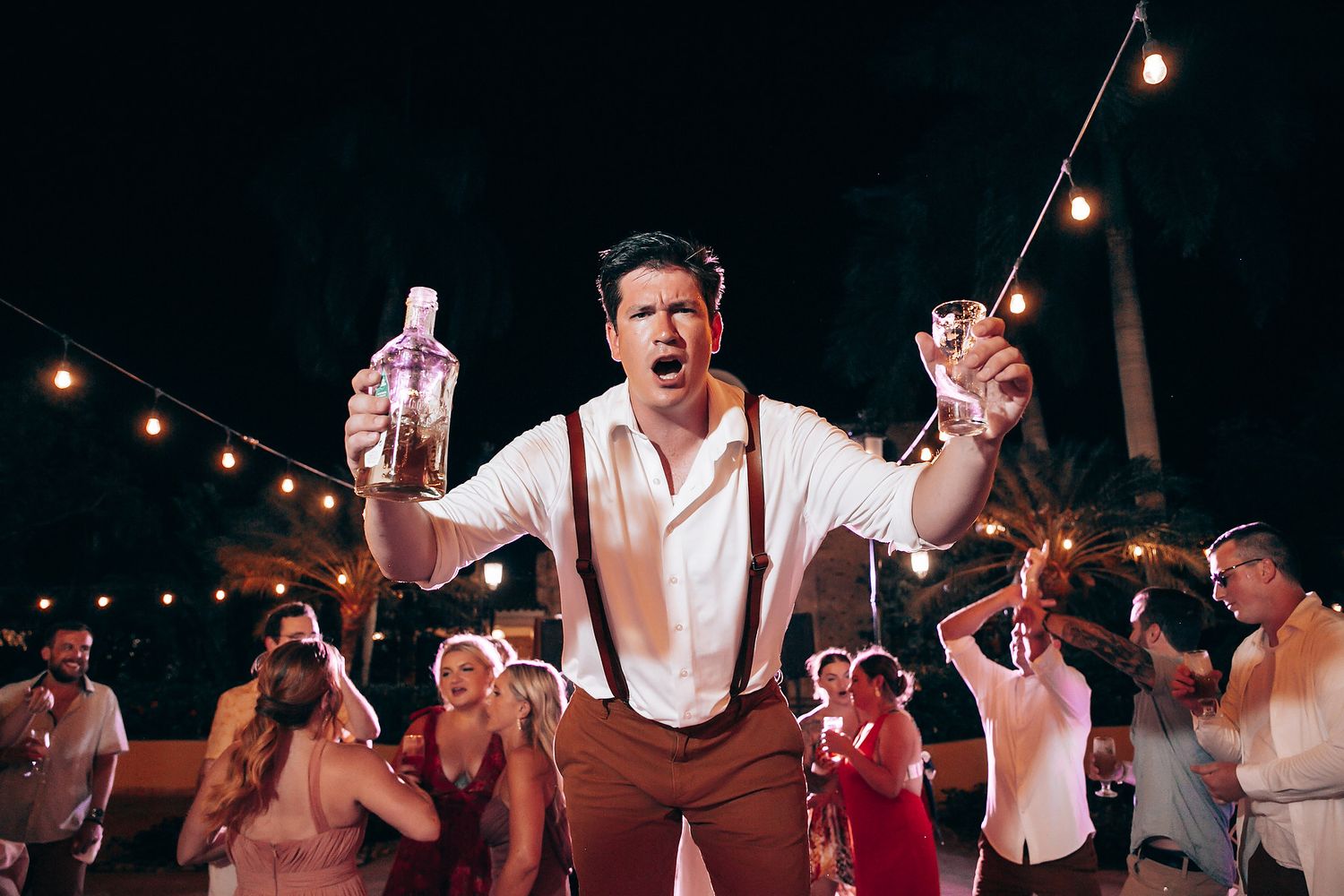 Wedding guests dancing and celebrating under warm string lights at night.