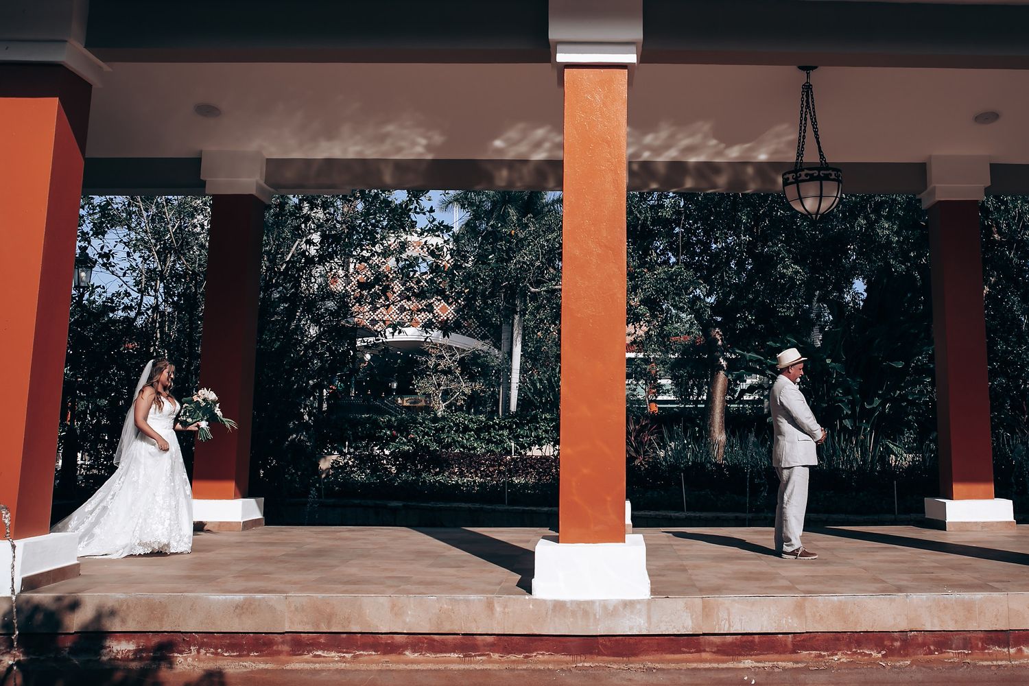 Wedding ceremony setup under an outdoor covered walkway with orange pillars and natural lighting.