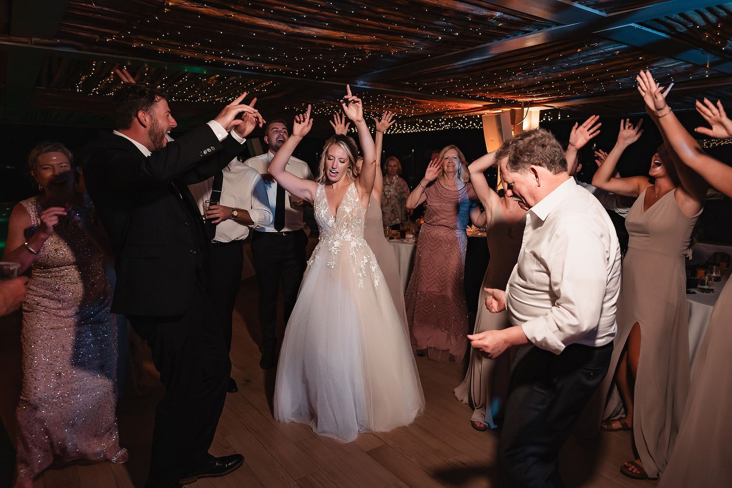 Wedding guests dance and celebrate on a dimly lit dance floor during the reception.