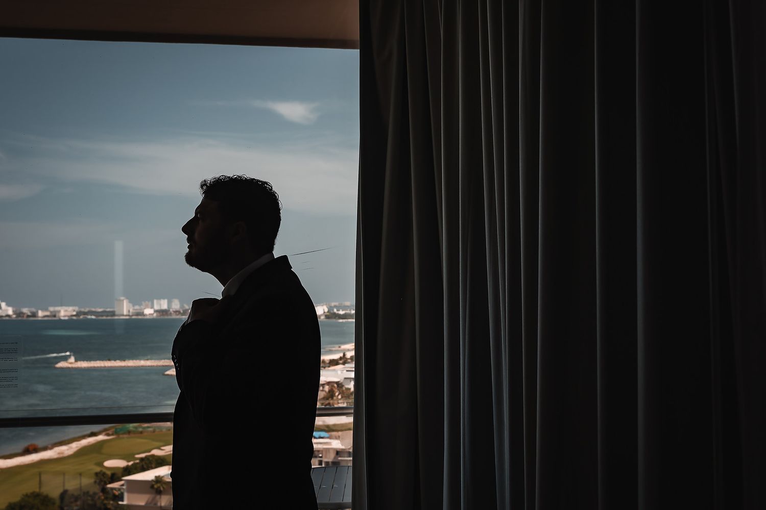Silhouette of a person standing by a window with ocean and ships visible in the distance.