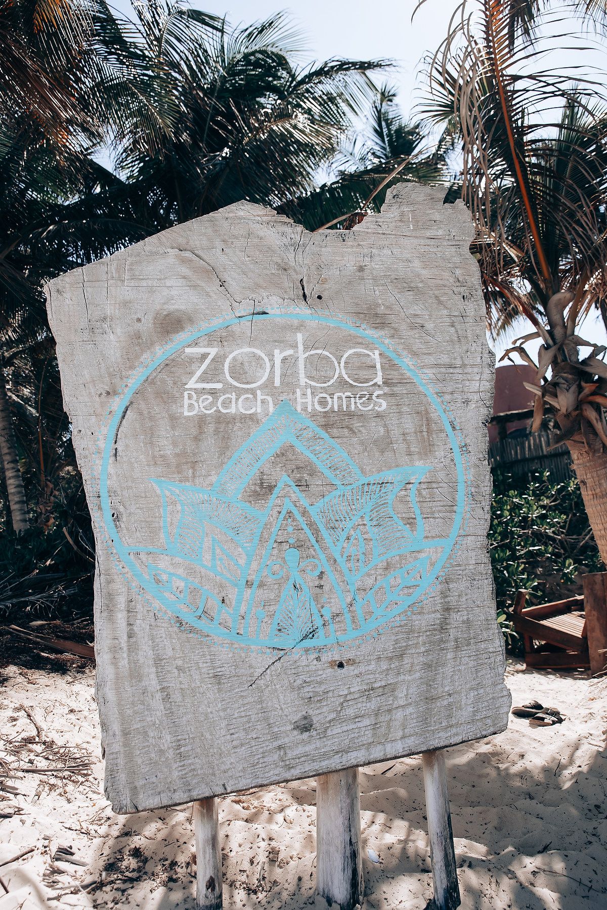 A sequence of beachside signs with light blue text painted on weathered concrete walls among palm trees.
