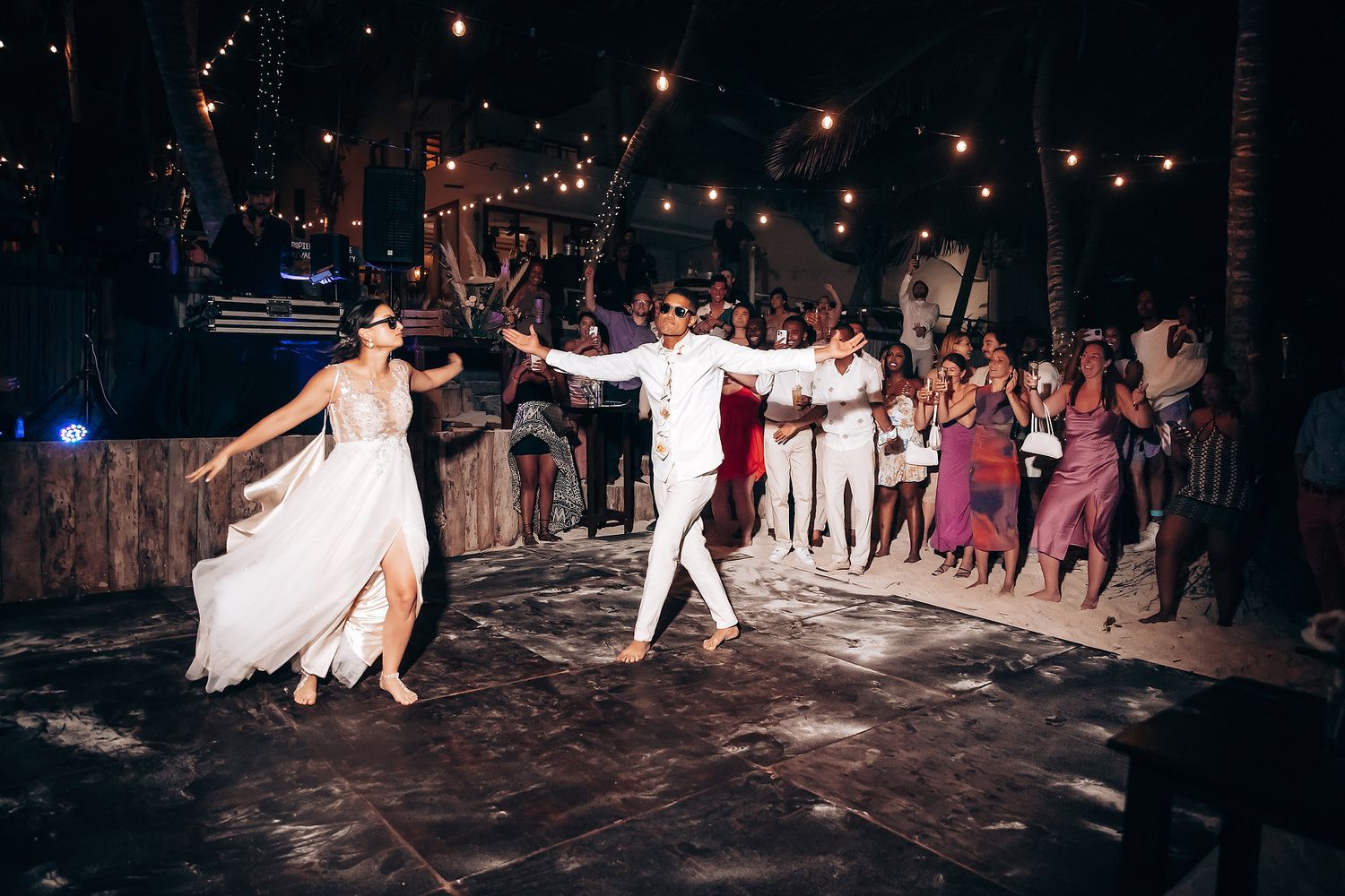 Evening wedding reception with guests dancing under string lights on outdoor dance floor.