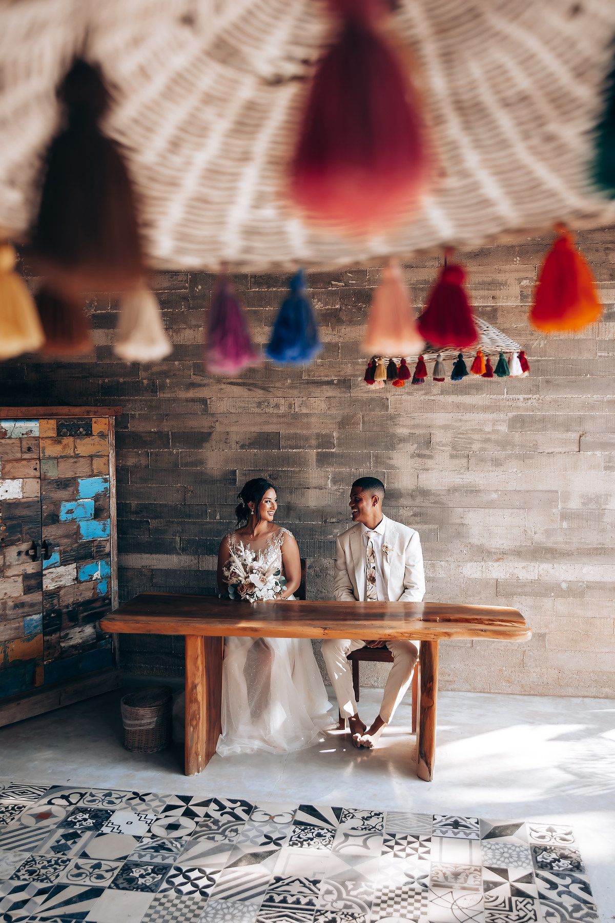 Rustic wedding venue with colorful tassels hanging from wooden beams and patterned floor tiles.