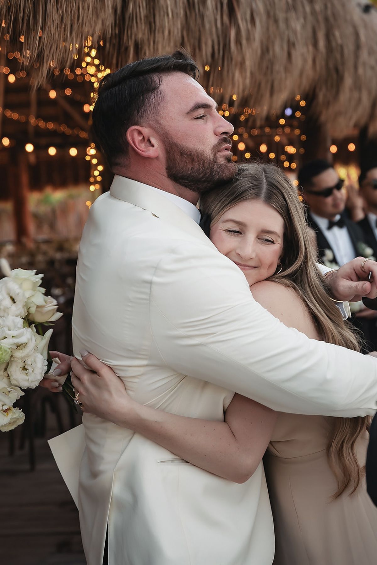 Bride and groom share a heartfelt hug at their outdoor wedding reception under warm string lights.