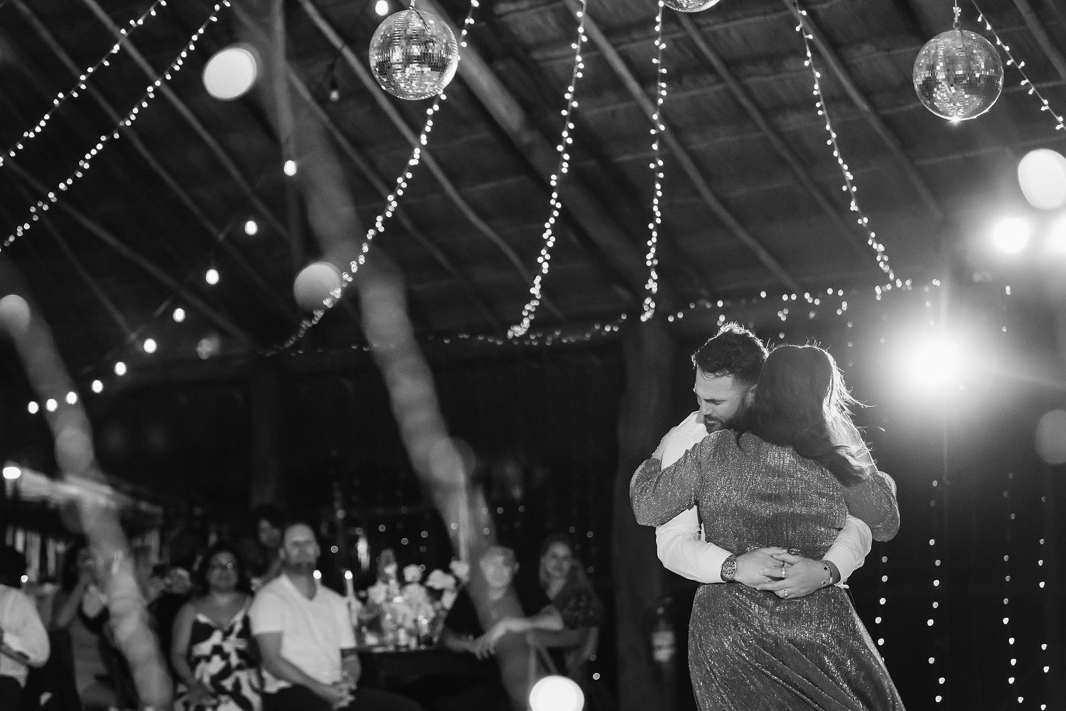 Couple shares their first dance under twinkling string lights and disco balls at a romantic wedding reception.