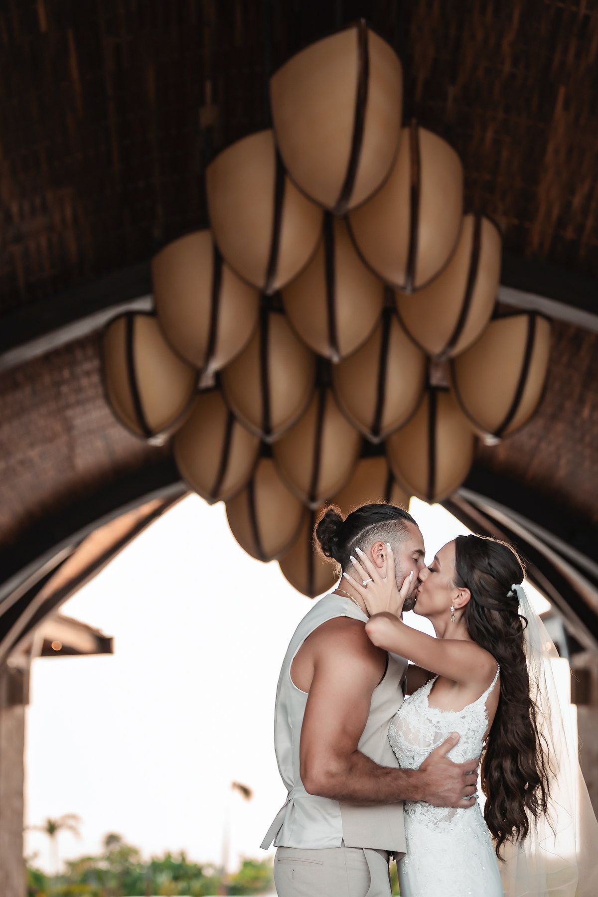 Bride and groom share a romantic kiss under decorative lanterns at an outdoor wedding venue.