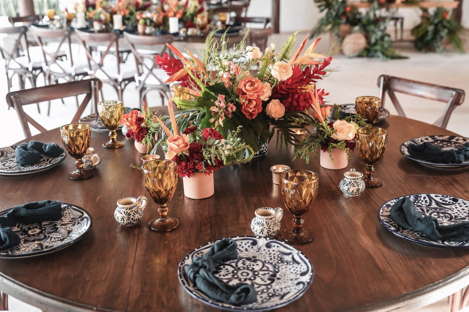 Elegant round wedding table with floral centerpiece, amber goblets, black damask plates, and dark napkins on a wooden table.