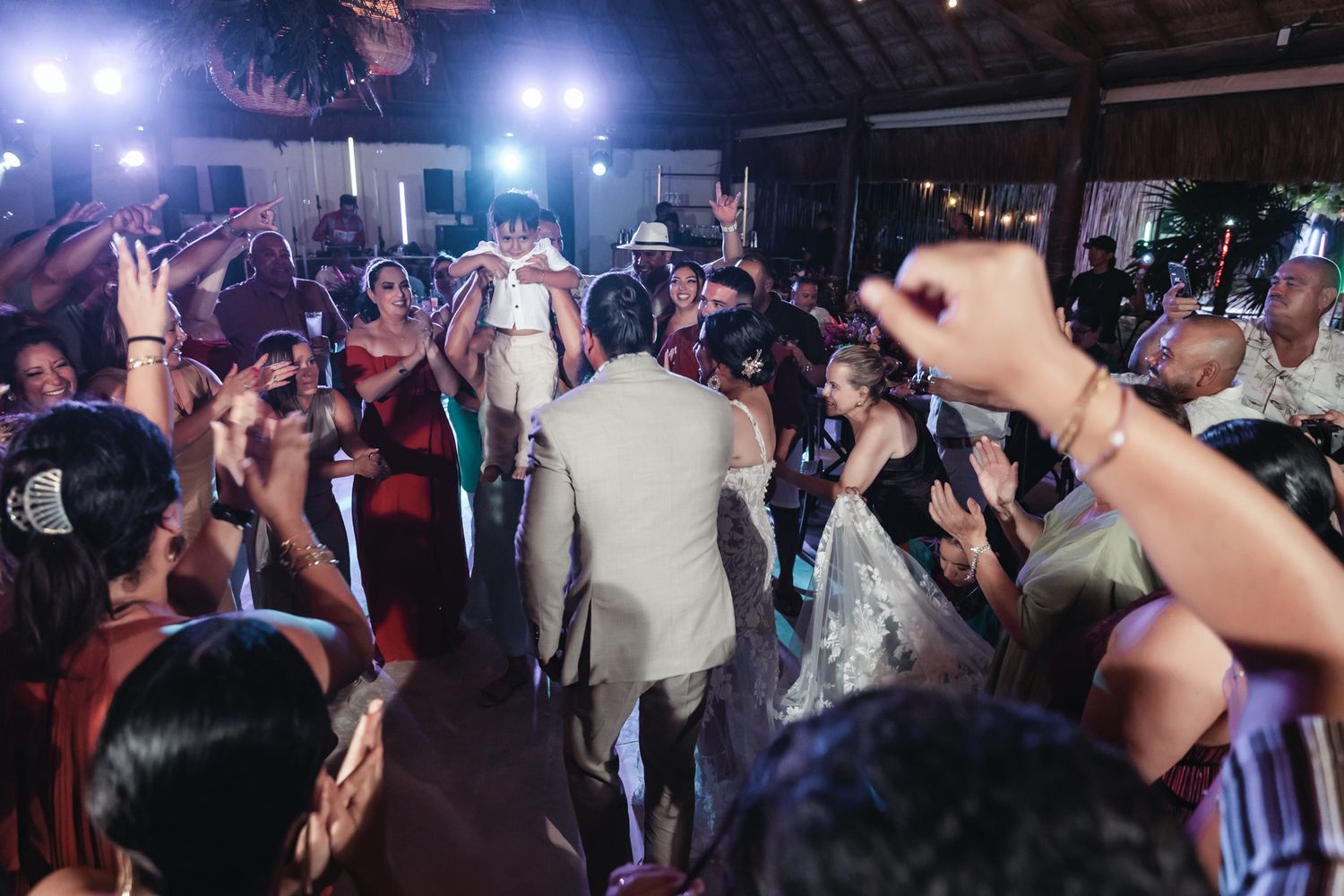 Bride and groom share a joyful first dance surrounded by celebrating wedding guests at a tropical outdoor reception.