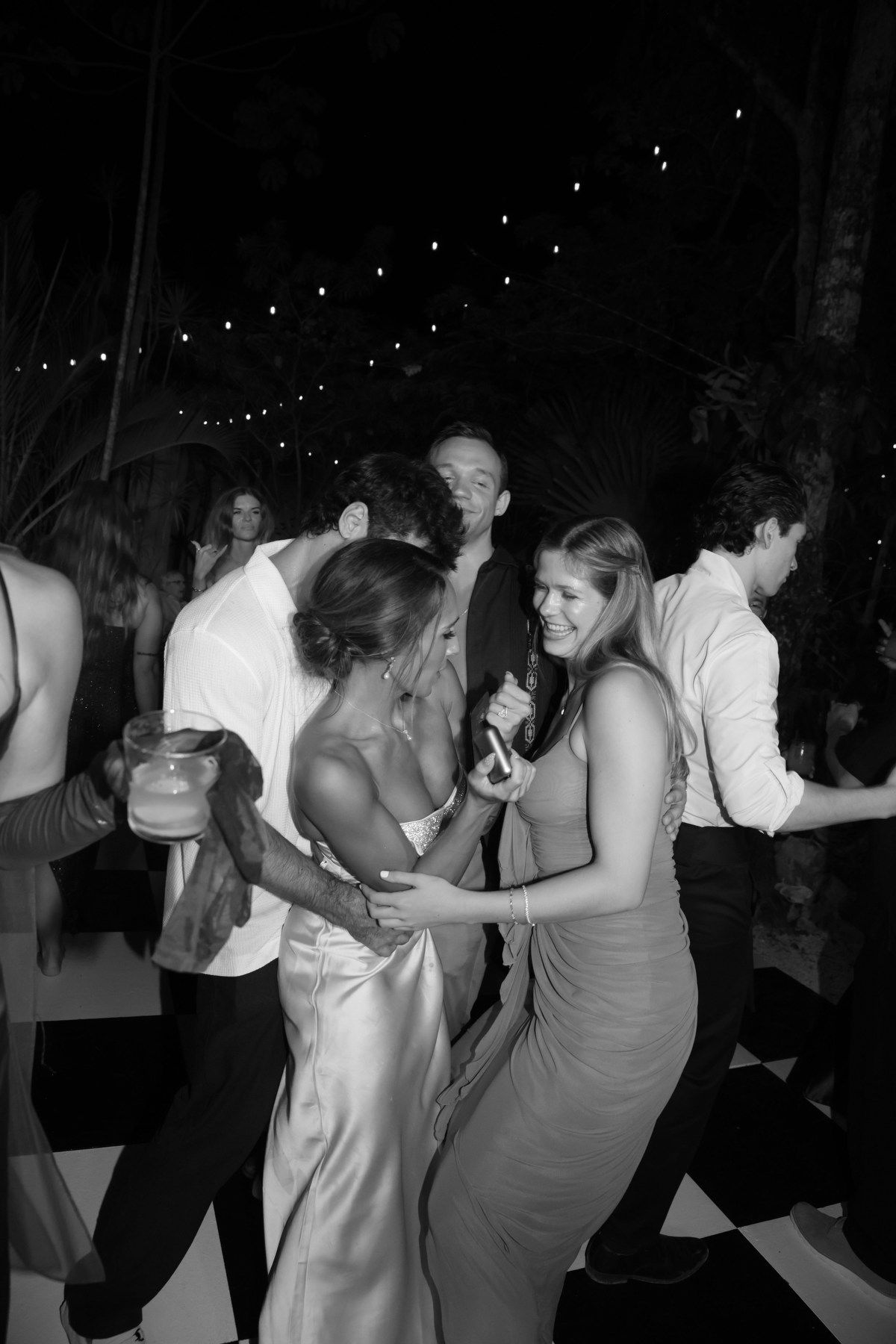 Guests dancing joyfully at an outdoor wedding reception in black and white photography.