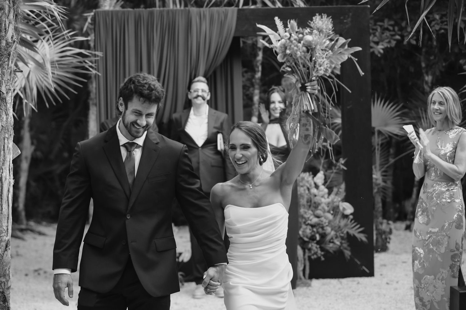 Black and white photo of a joyful bride and groom walking after their outdoor wedding ceremony.