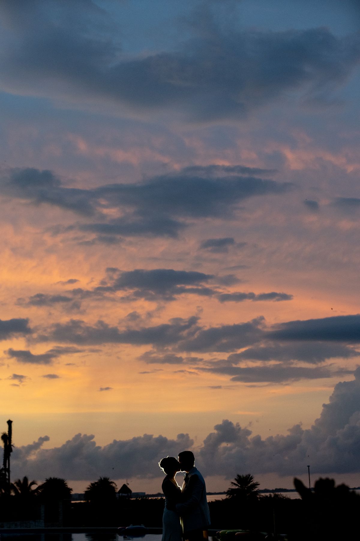 Silhouette of a couple kissing against a dramatic pink and purple sunset sky with clouds.
