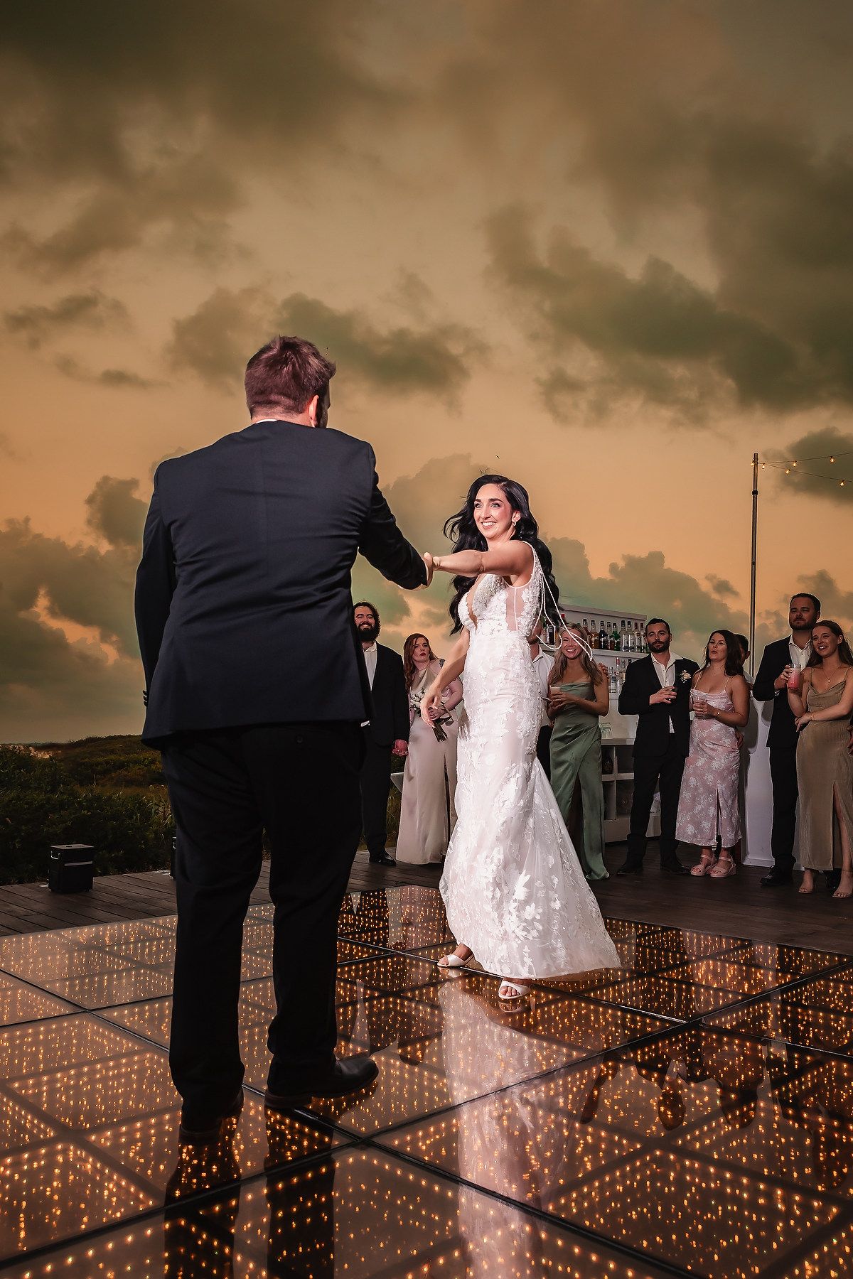 Wedding couple dancing on illuminated floor during sunset reception.