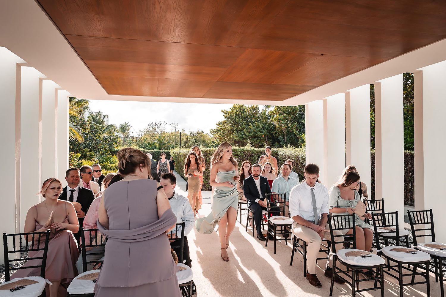 Wedding party members in formal attire gather under a covered outdoor venue with white columns.