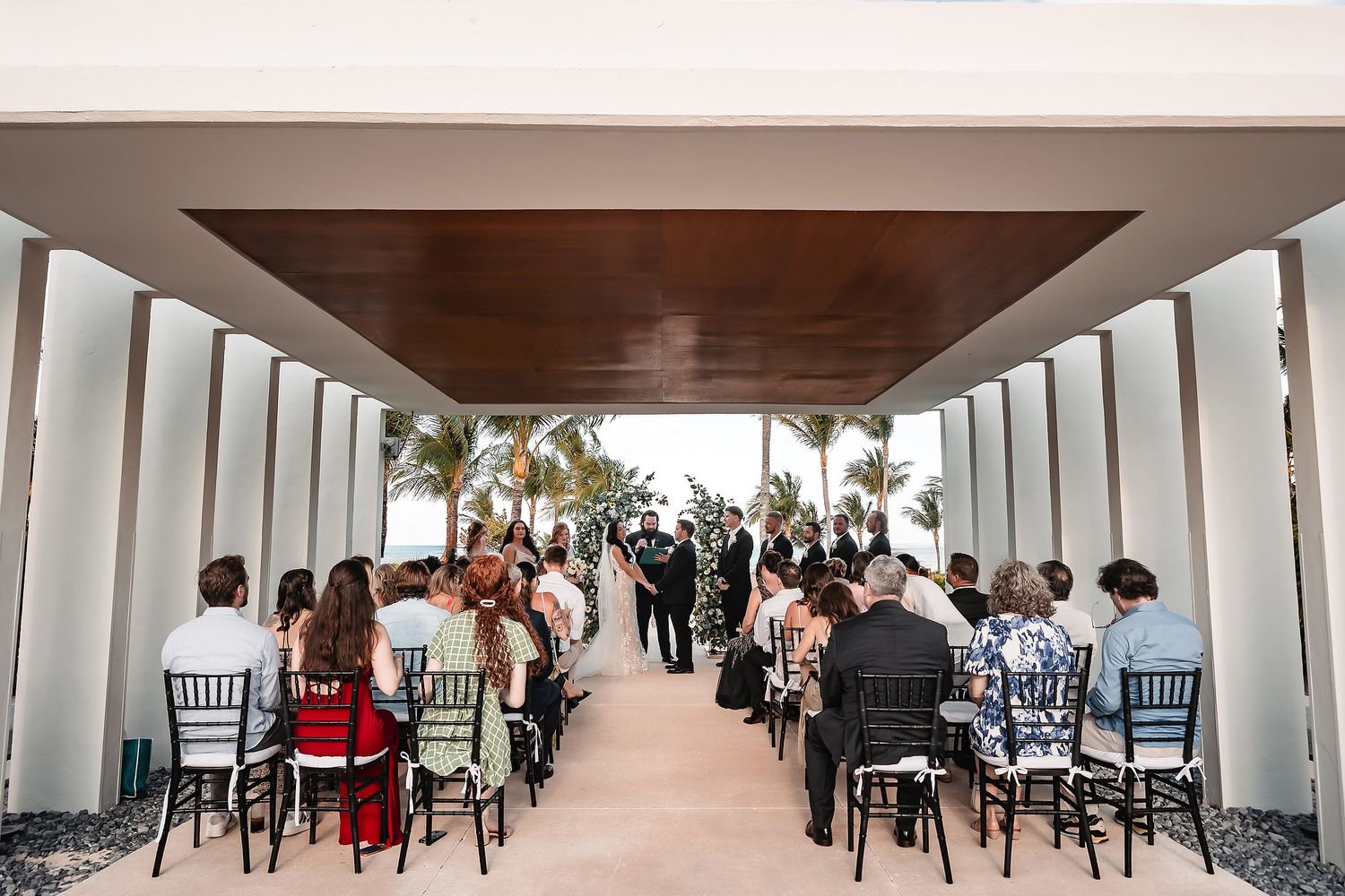 Long hallway at wedding venue with elegant white decor and black chairs lined up on both sides.