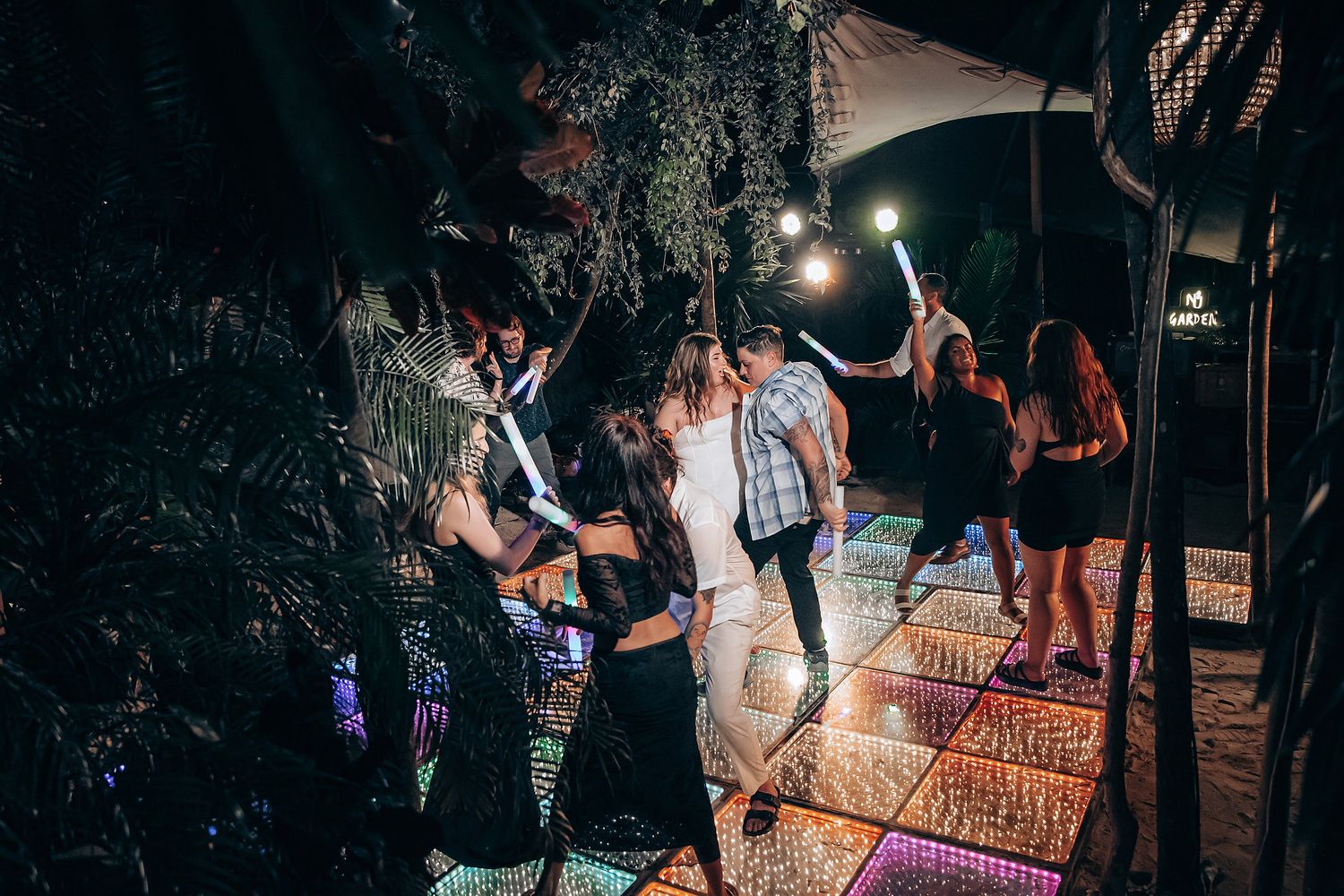 A lively nighttime dance party on an outdoor deck with string lights and people dancing and having fun.