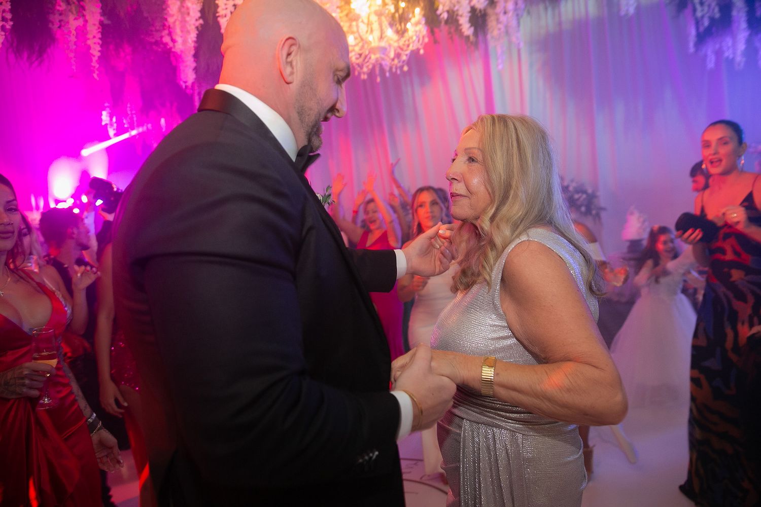 Couples dancing together at a wedding reception with pink and purple lighting creating a romantic atmosphere.