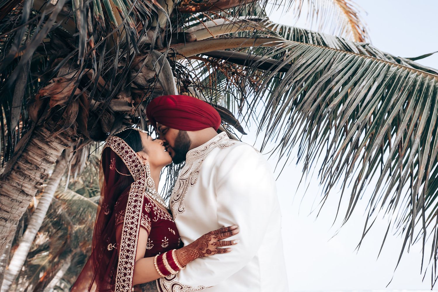 Tropical palm fronds create natural canopy over beach wedding setting.