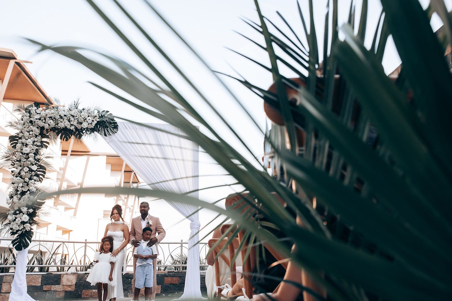Palm fronds frame an outdoor wedding ceremony setting with white drapes.