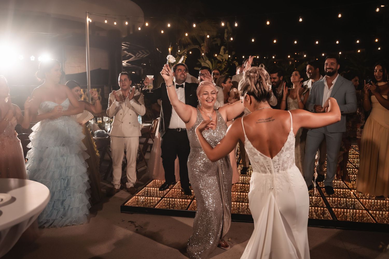 Wedding celebration with guests dancing under romantic string light decorations at night.