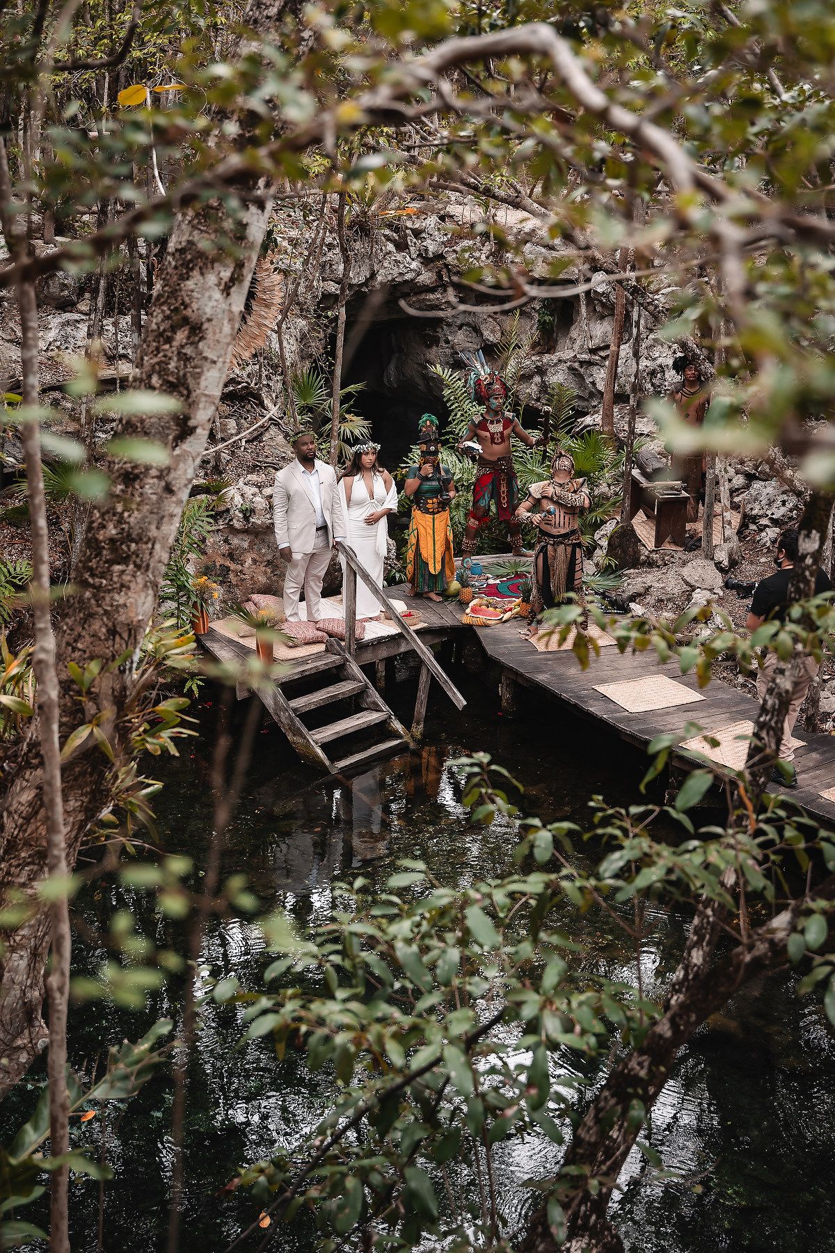 Ancient cave entrance with ceremonial decorations and wooden platform over turquoise waters.