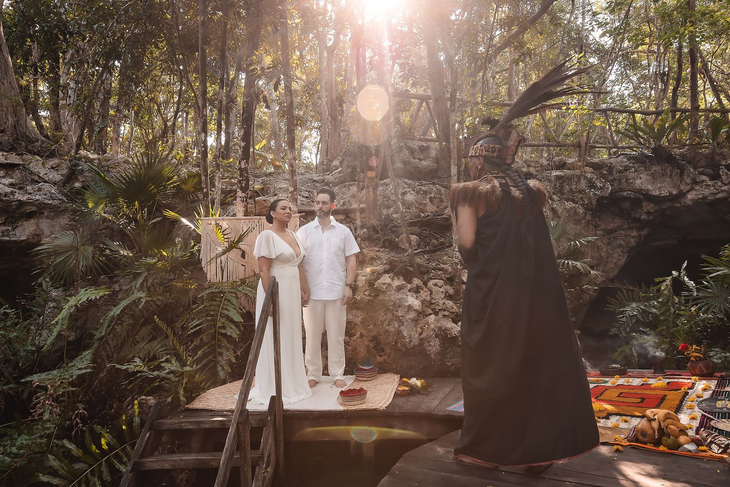 Sunlit outdoor wedding ceremony in a natural stone grotto with traditional Mayan elements.