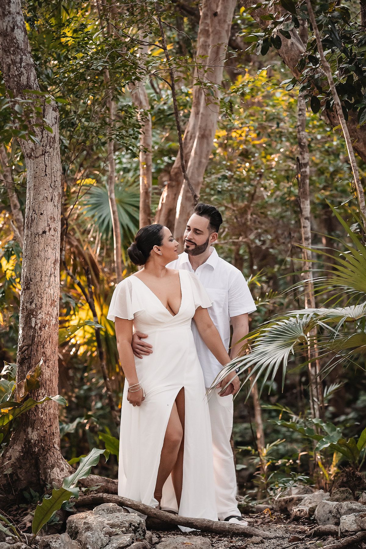 A couple shares an intimate moment while standing on rocks in a tropical forest setting.