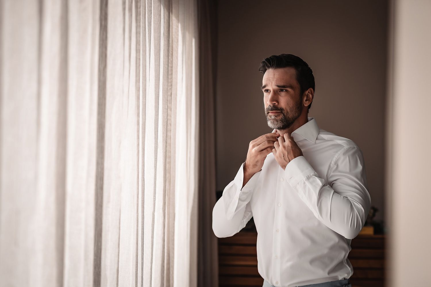 Groom preparation sequence showing collar adjustments in window light.