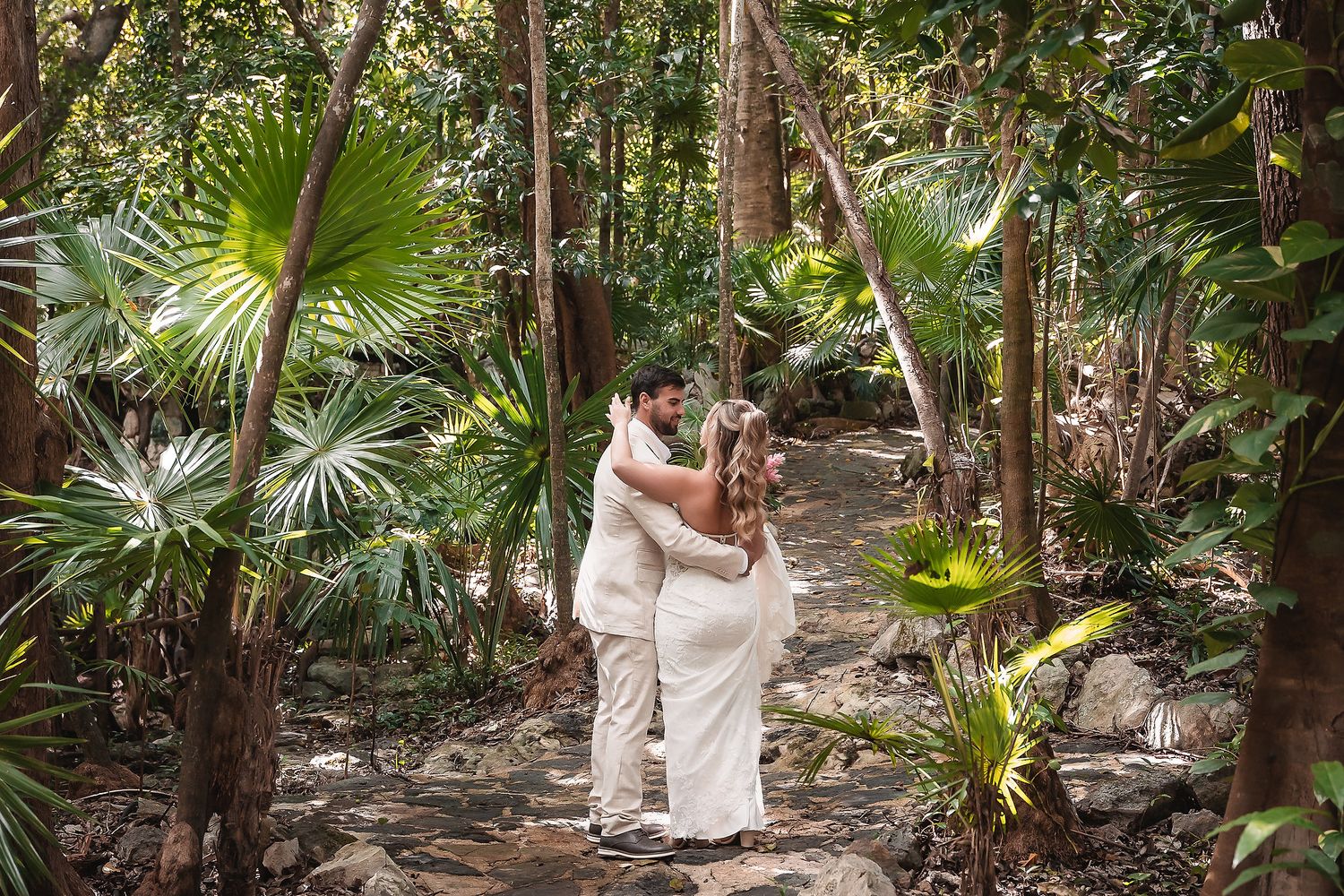 Wedding couple strolling along a stone path surrounded by tropical foliage.