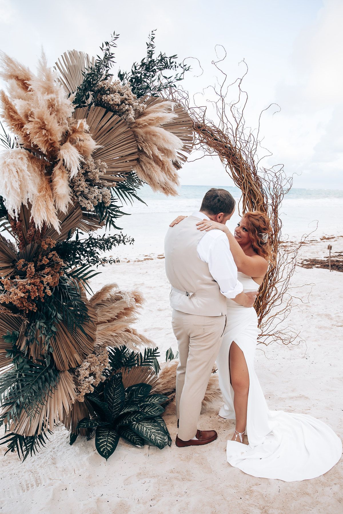Bohemian beach wedding arch decorated with pampas grass and tropical greenery.