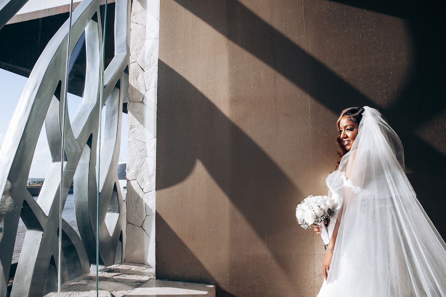 A flowing white wedding dress creates elegant shadows against a neutral wall.