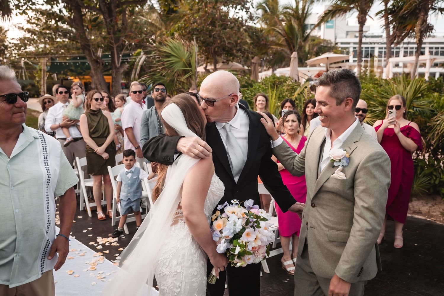Outdoor wedding celebration with guests gathered under tropical palm trees.