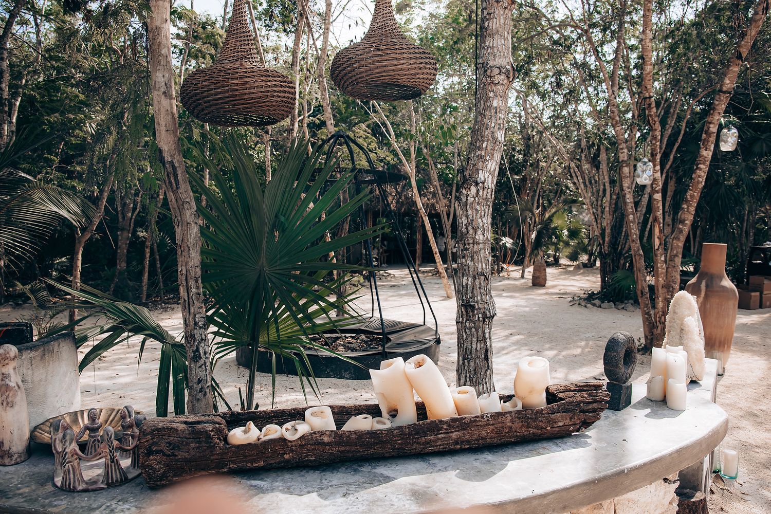 Outdoor wedding venue decorated with hanging lights and white candles among natural trees.