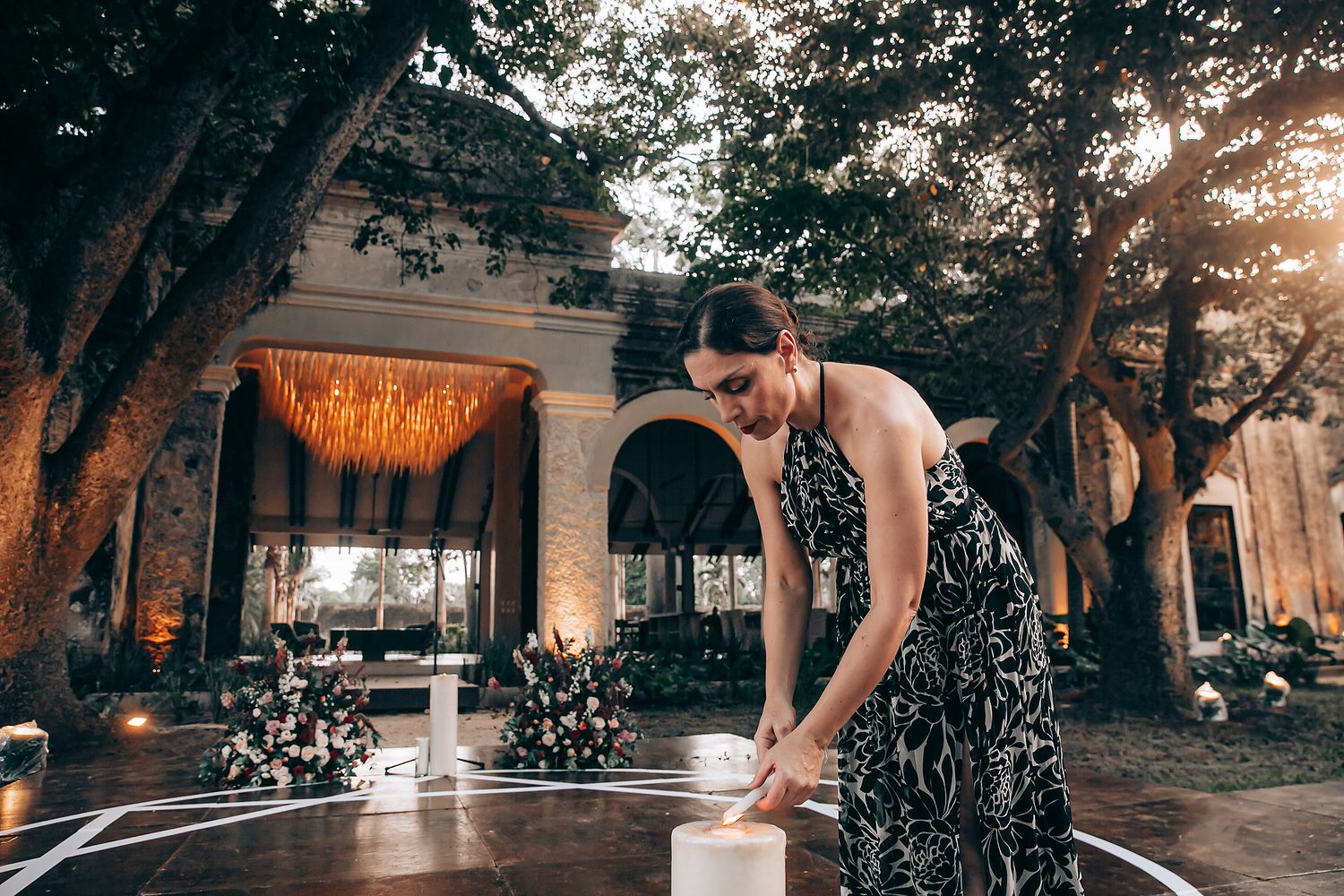 Person in floral dress bending down to touch water in a fountain at sunset with ornate architecture in background.