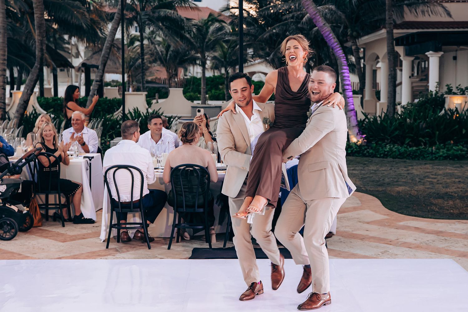 Wedding guests dancing and celebrating on an outdoor dance floor during a sunset reception celebration.