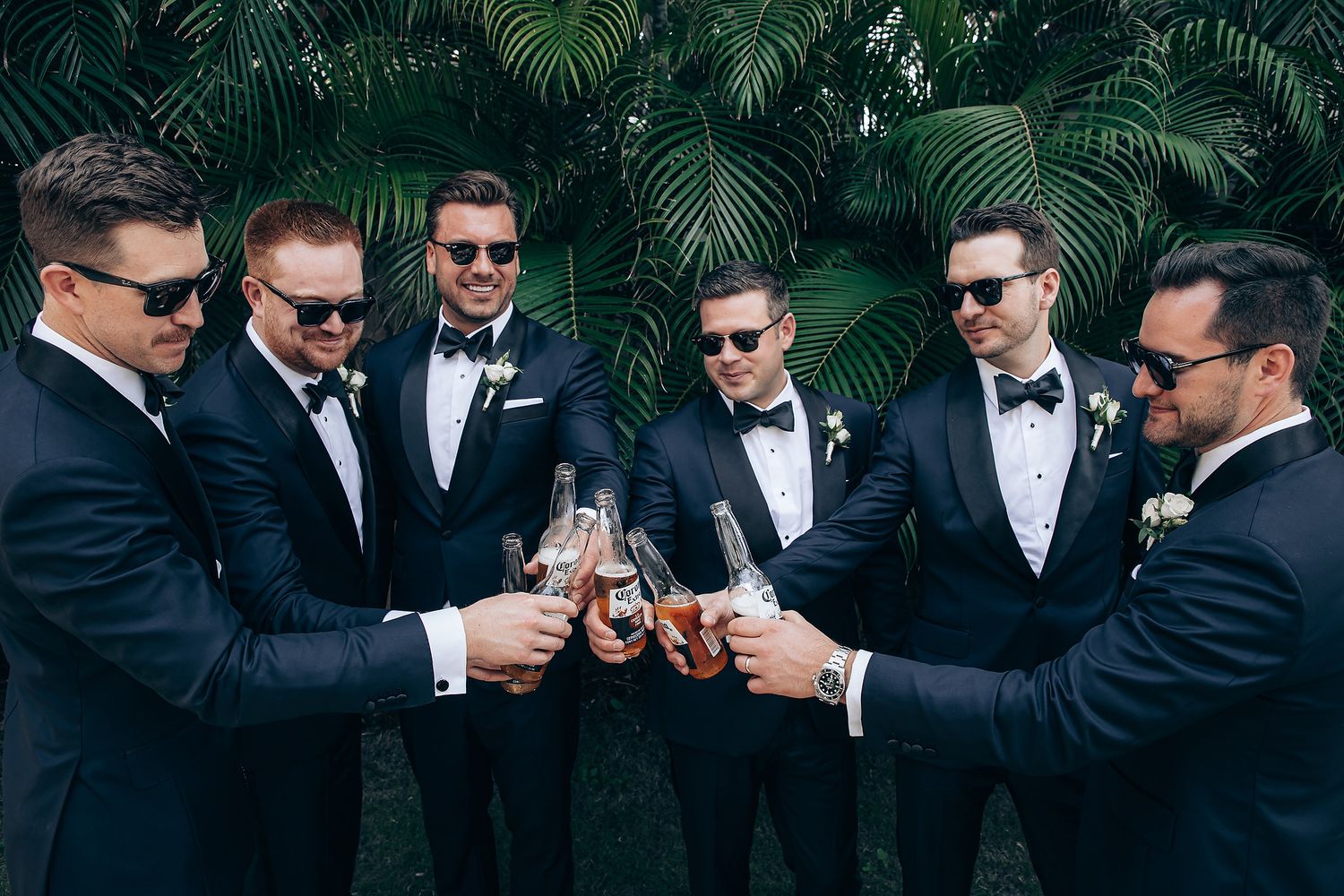A group of groomsmen in black suits and sunglasses pose together in a cinematic style for wedding photos.