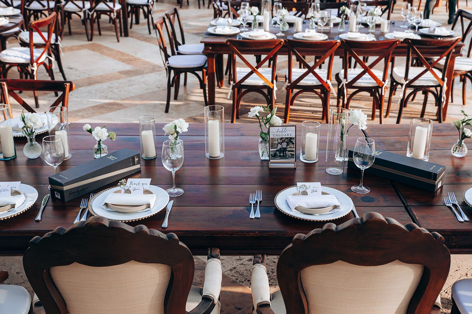 Empty restaurant tables with white tablecloths and wooden chairs set up in a dining room with natural lighting.