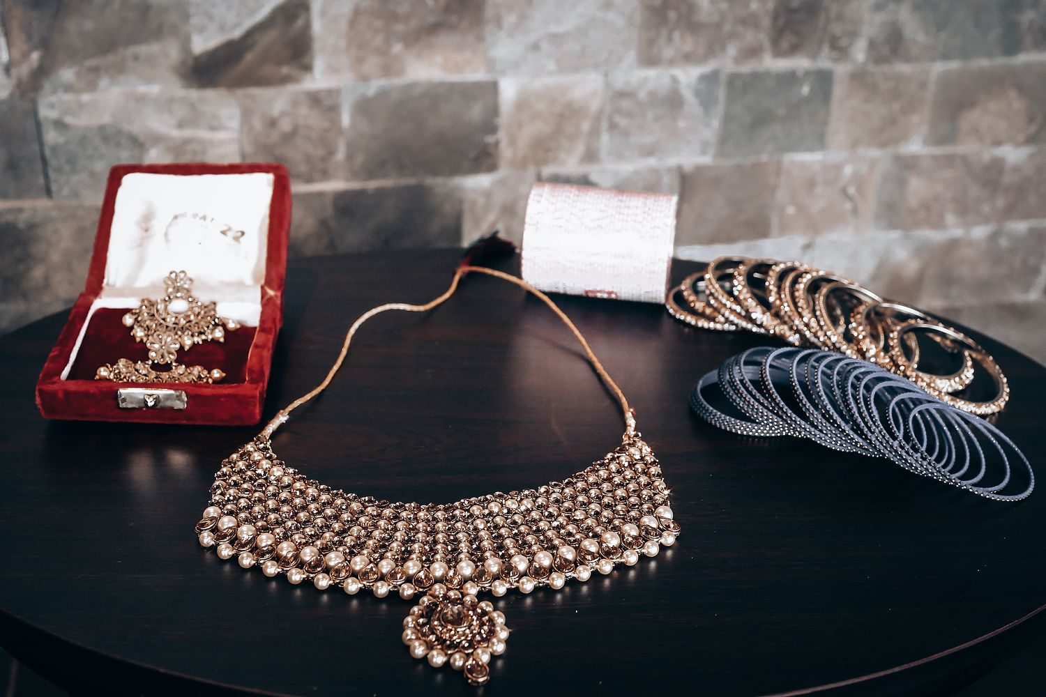 Traditional Indian bridal jewelry including an ornate gold choker necklace and bangles displayed on a dark surface.
