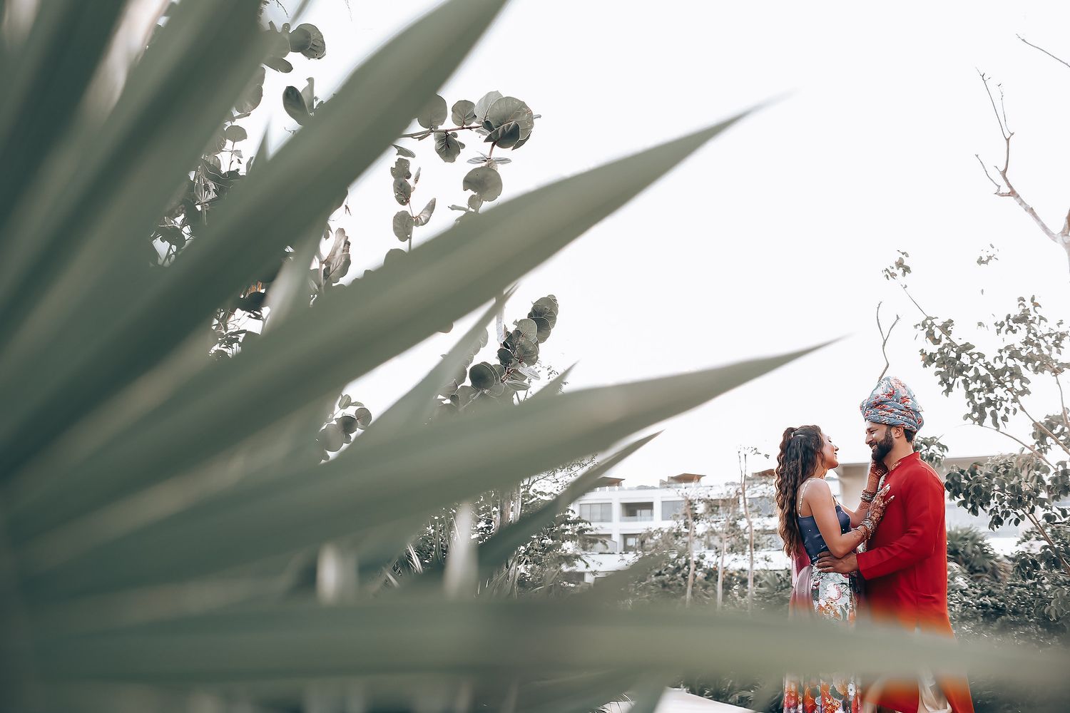 A person in a red jacket stands on a balcony with palm fronds visible in the foreground.