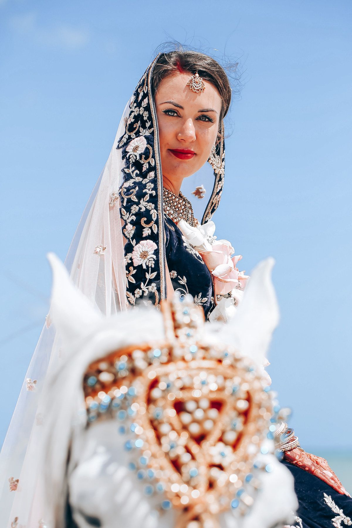 Close-up details of bridal jewelry and veil against bright blue sky backdrop.