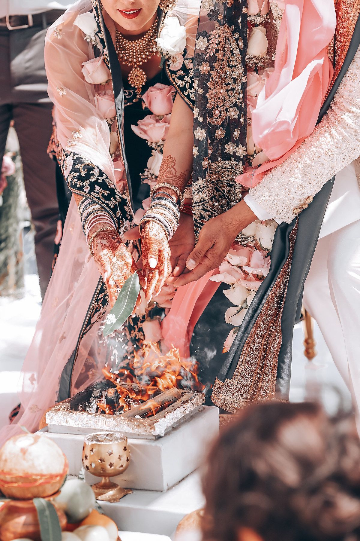 Close-up view of traditional Indian wedding ceremony with hands performing rituals over decorated items and flowers.