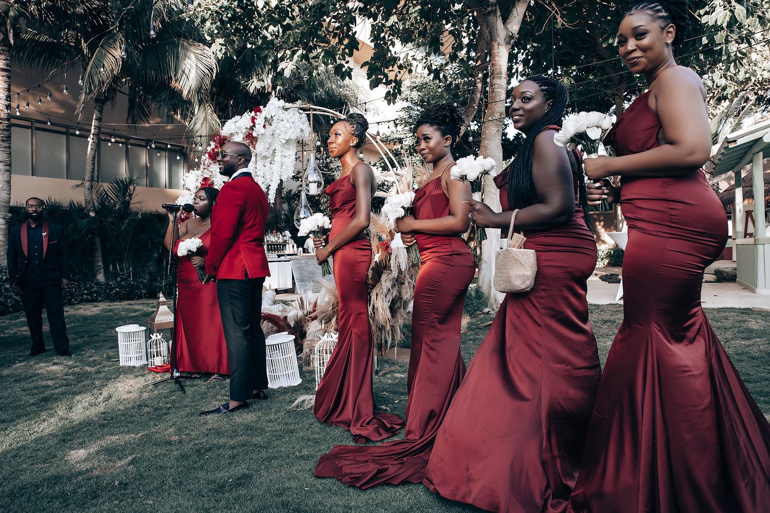Bridesmaids in burgundy dresses gather outdoors for wedding photos on a sunny day.