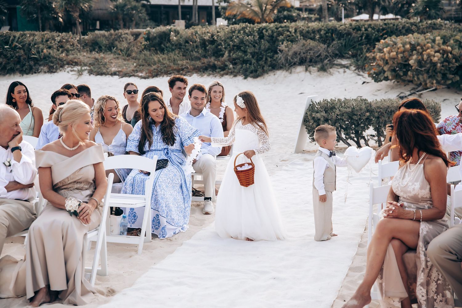 Wedding guests seated in white chairs on a beach for an outdoor ceremony.