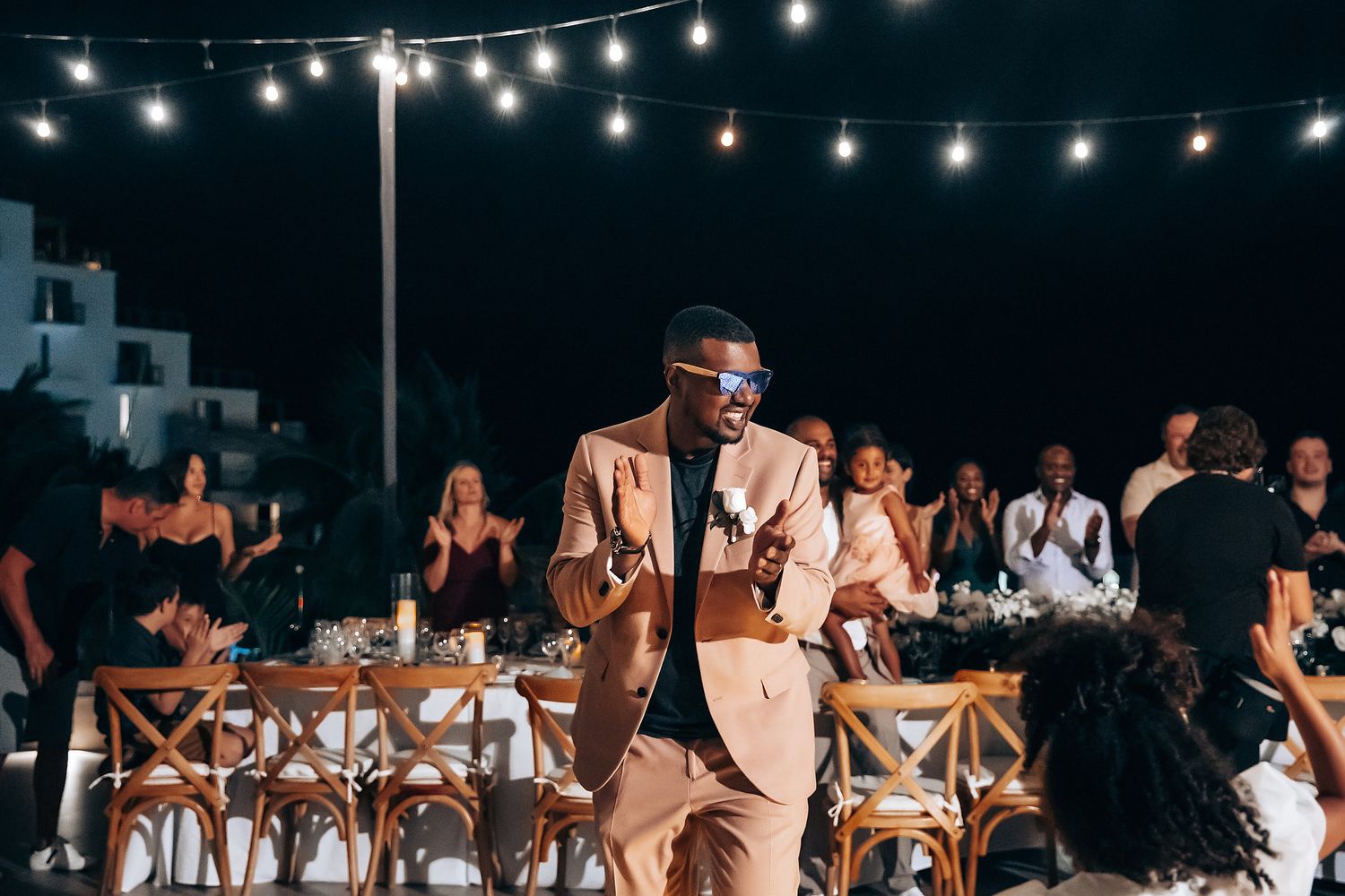 An outdoor wedding reception under string lights with guests seated at tables.