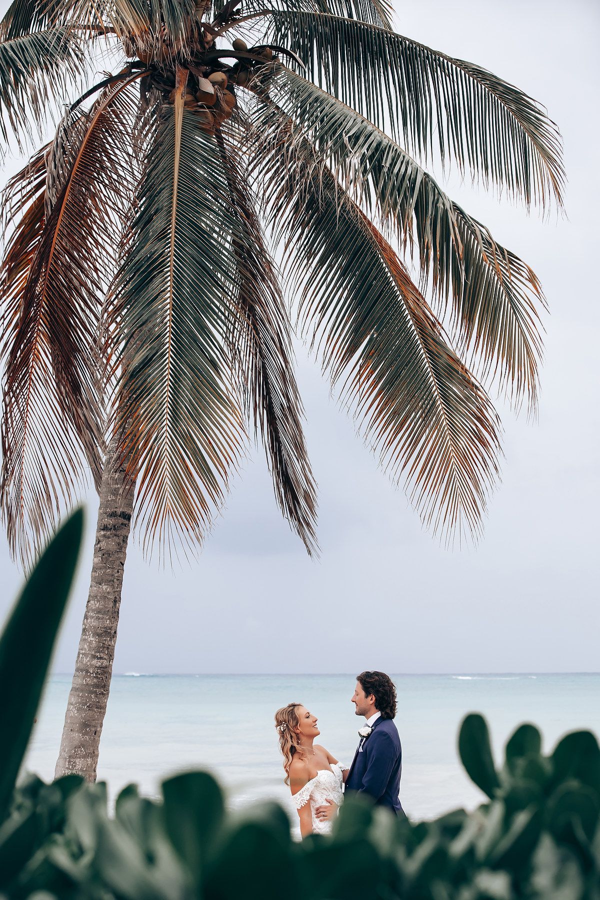 Romantic wedding moment under swaying palm trees with ocean backdrop.