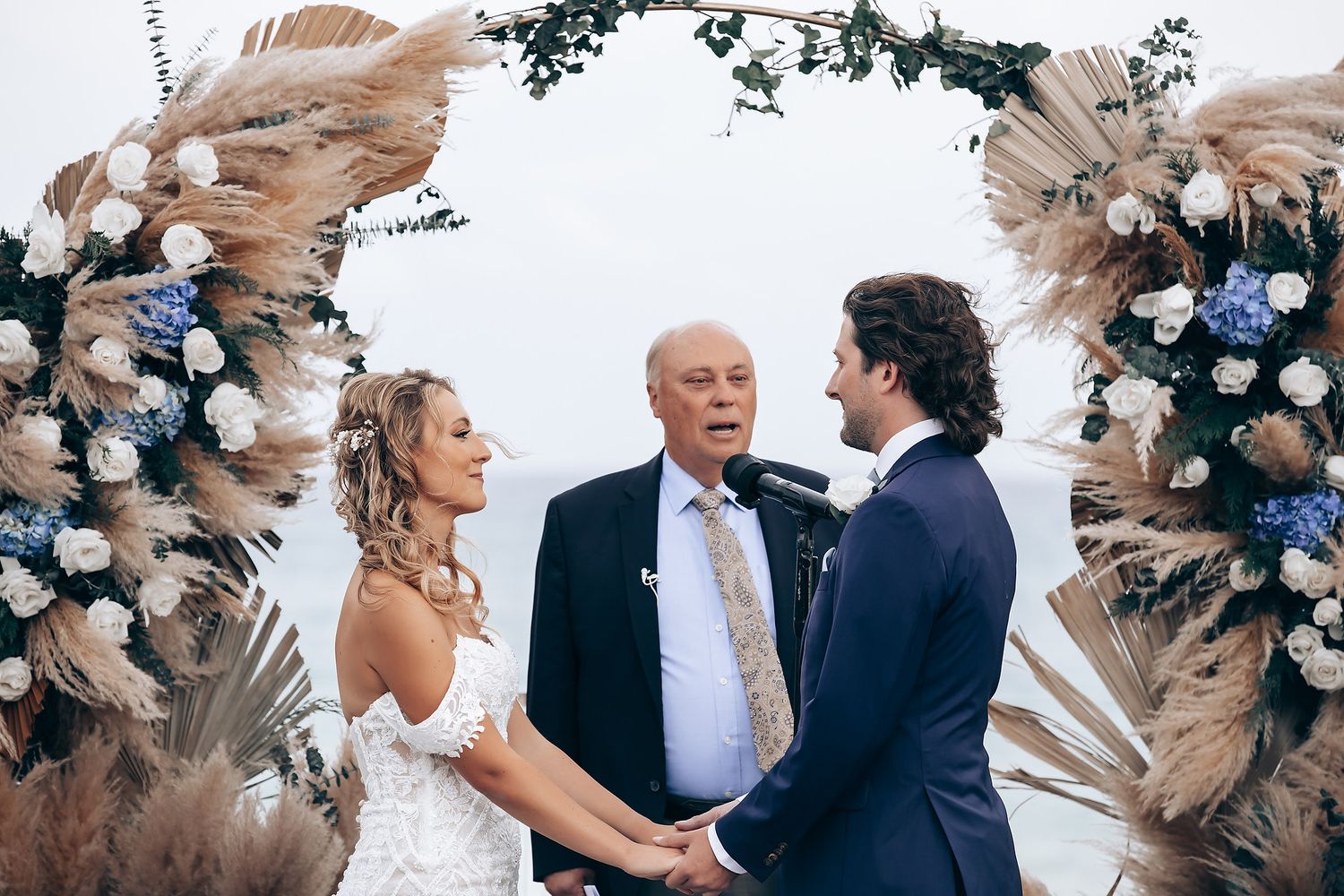 Wedding ceremony scene with boho floral arch and gathered guests.
