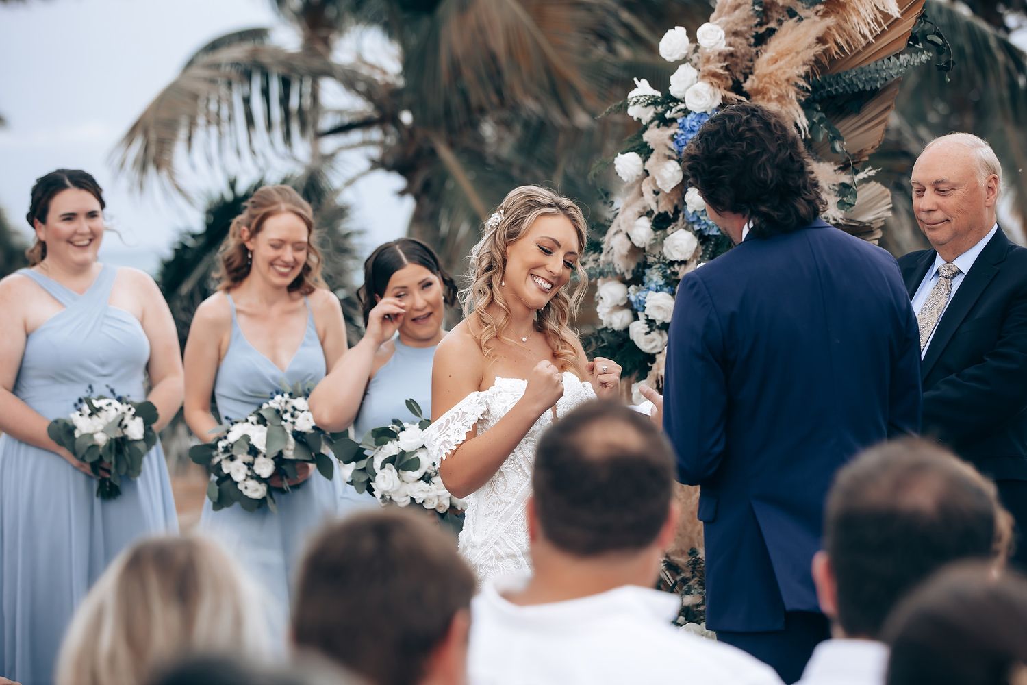 Wedding party celebrating on a wooden deck overlooking the ocean with palm trees swaying in the breeze.