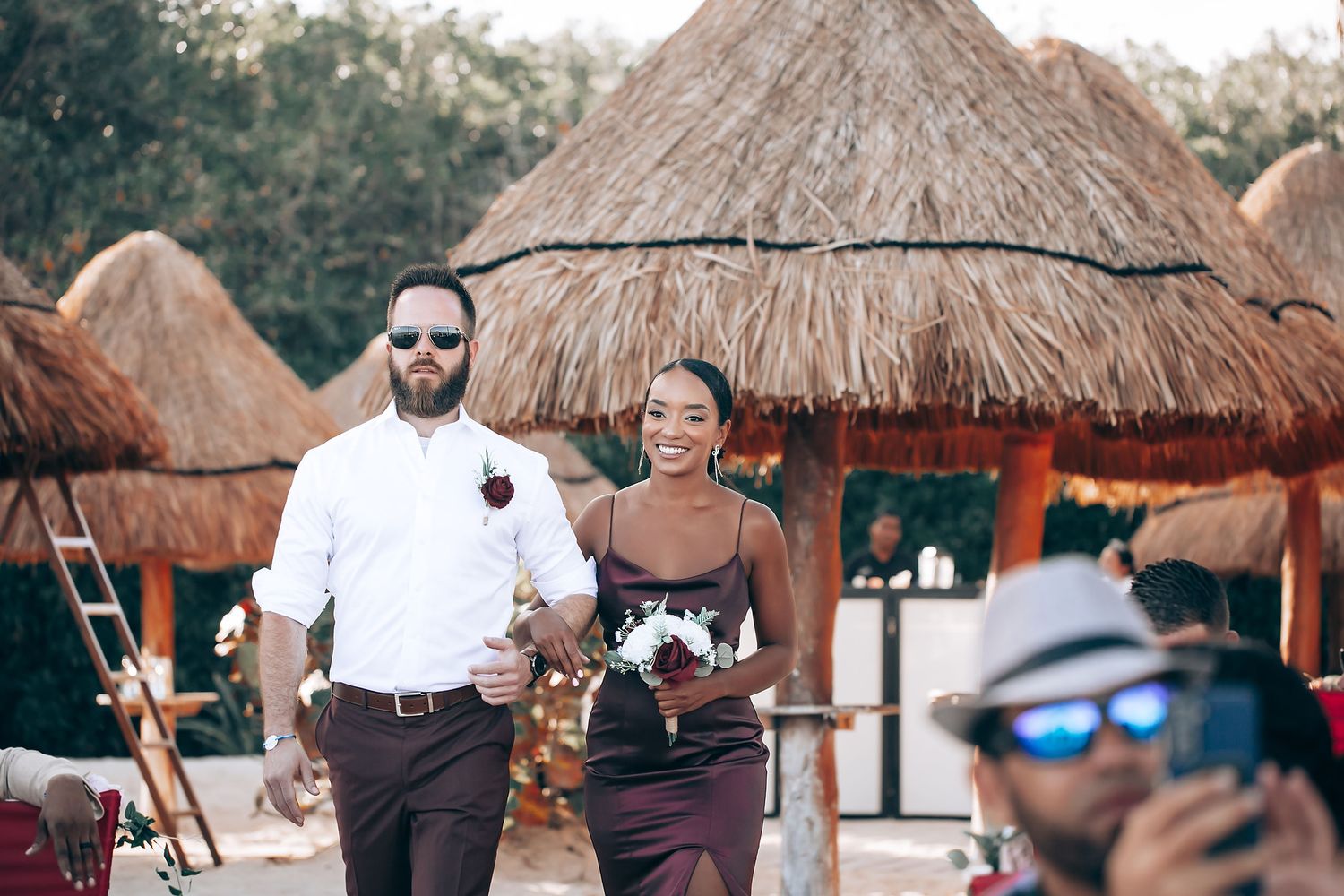Destination beach wedding ceremony setup with thatched roof palapas and chairs on tropical sand.